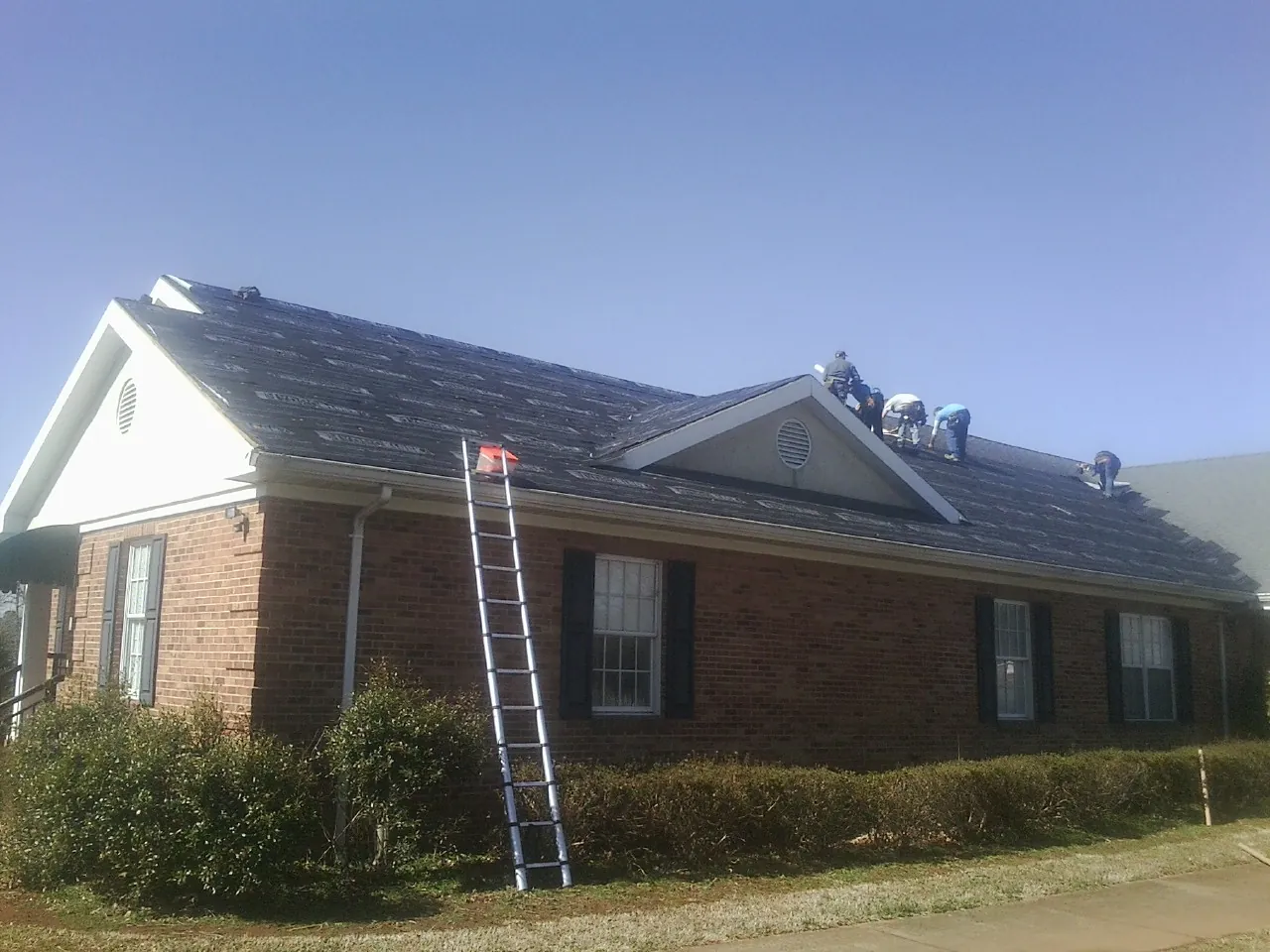 Crew tearing shingles off a brick ranch roof with a ladder set — Metal Roof Repair work by our crew in Cottontown