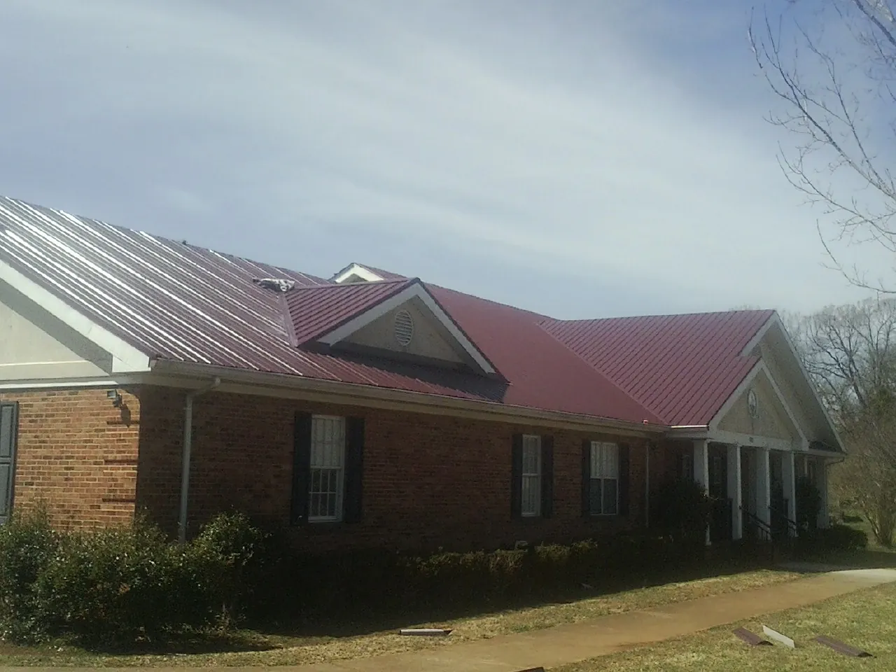 Red metal roof with gabled entries on a long brick building, from a Hail Damage Roof Repair job in Cottontown