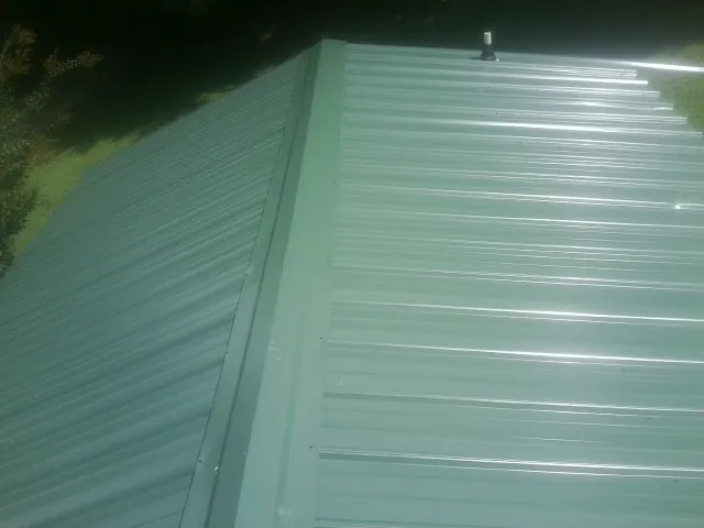 New green metal panels meeting at the ridge of a roof — Flat Roof Repair work by our crew in Cottontown