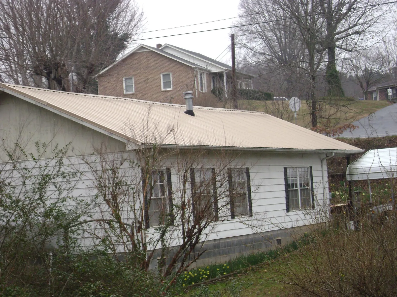 Tan metal roof on a white sided house set into a hillside — Commercial Roofing by Roofing Brothers in Cottontown